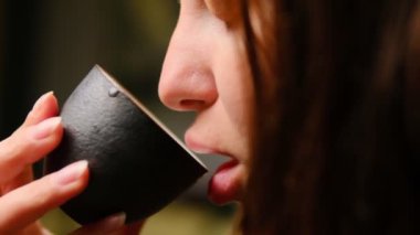 Siyah bir seramik bardaktan çay yudumlayan dudakların detaylı görüntüsü gelenek ve farkındalığı vurguluyor..