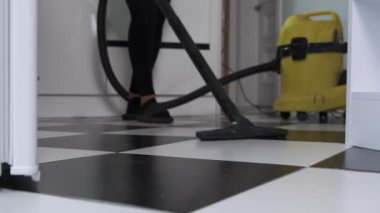 Mutfak zemininde elektrikli süpürge kullanan siyah beyaz fayanslı, toz ve kiri temizleyen bir kadının yakın çekimi..