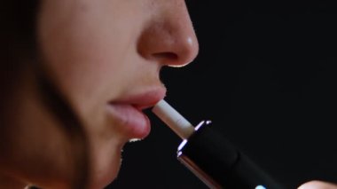 Arka planda elektronik bir sigaradan buhar üfleyerek nefes alan bir kadının yakın çekimi..