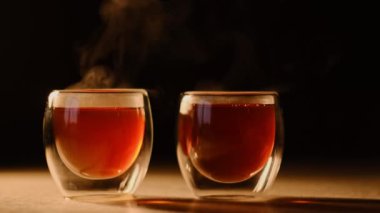 Koyu arkaplanda buharı tüten iki çay fincanı. Ilık ışık, aromatik buharı vurguluyor. Çay temalı içerik üzerine metin kaplaması için mükemmel.