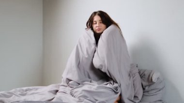 Soğuk, gri bir odada bir kadın bir battaniyenin altına saklanır, depresyon ve duygusal mücadeleler altında ezilir..
