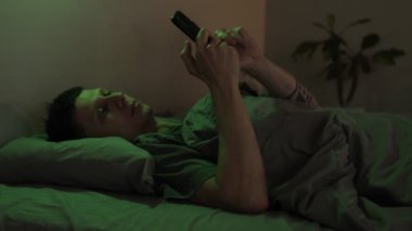 Sıcak bir odada, rahat bir odada akıllı telefon kullanarak akıllı ışıklandırmayı kontrol eden ve renkleri seçen, modern teknolojiyi sergileyen bir adam..
