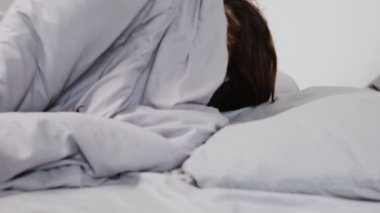 Genç bir kadın soğuk, gri bir odada depresyon ve zihinsel zorluklarla boğulmuş bir şekilde battaniyenin altına saklanıyor..