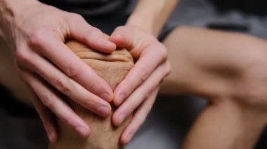Evdeki bir adam eklem ağrısından ve sağlığına dikkat etmek için dizine masaj yapıyor..