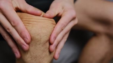 Bir adam eklem ağrısını hafifletmek ve hareket kabiliyetini arttırmak için dizine evde masaj yapar..
