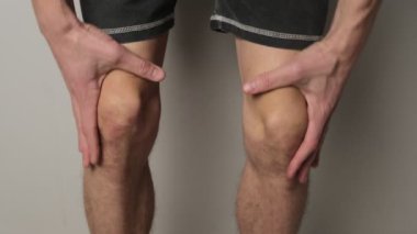 Adam iki eliyle dizlerine masaj yapıyor, eklem bakım ve ağrı kesicilere odaklanıyor. Eklem ağrısı ve koruyucu masaj kavramı.
