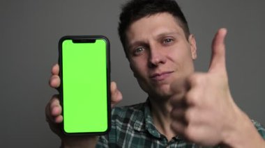 Bir adam yeşil ekranda kendine güvenen bir ifadeyle telefon modeline işaret eder. Tavsiye etmek için işaret eder, reklam konseptini somutlaştırır ve bir stüdyo ortamında promosyon yapar.