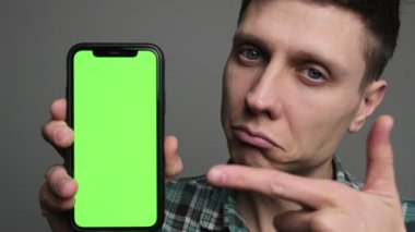 Bir adam yeşil ekranlı akıllı bir telefonu işaret eden bir ürün öneriyor. Stüdyo geçmişine karşı reklam ve pazarlama için ideal. Yüksek kalite 4k görüntü