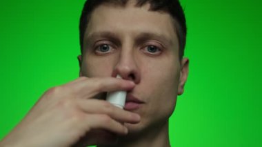 Siyah kazaklı ve kırmızı sakallı genç bir adam burnuna püskürtüyor. Kaydırağın yakın çekimi..