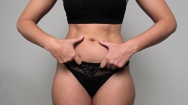 Kadın şişman karnına dokunuyor. Kilo verme ve kilo verme kavramı. Stüdyonun gri arka planına yaklaş.