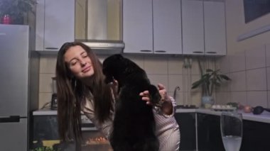 Mutfakta siyah kedisiyle dans eden genç ve güzel bir kadın..