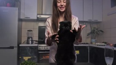 Mutfakta siyah kedisiyle dans eden genç ve güzel bir kadın..