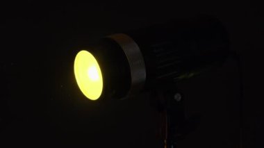 Stüdyo ışıkları karanlık bir ortamda güçlü bir sarı ışık yayar dramatik ve odaklanmış bir parıltı yaratır..