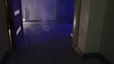 Yangın sırasında dumanlar bir daireyi dolduruyor, kapıdan sızıyor, arka planda itfaiye aracı ve ambulans ışıkları yanıp sönüyor. Yüksek kalite 4k görüntü