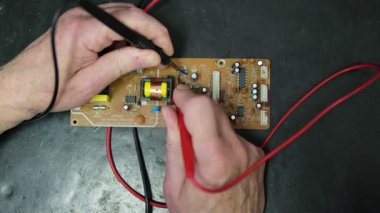 Devre kartını test etmek için çoklu metre kullanan bir elektrikçinin elleri voltajı ve tanı bileşenlerini kontrol eder..