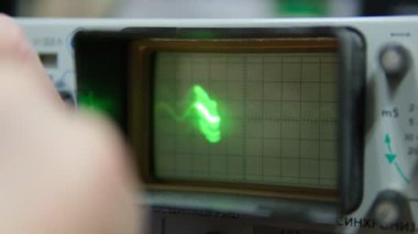 Retro osiloskop ekranının yakın görüntüsü hafif bulanık kenarlı, elektronik sinyal analizini gösteren parlak yeşil bir dalga formu sinyali gösterir.
