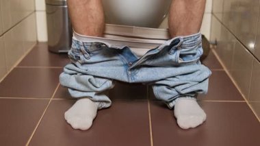 Tuvalette oturup tuvaleti kullanan bir adamın bacak ve ayaklarının bebeksi görüntüsü.