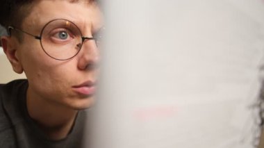 Yuvarlak gözlüklü genç bir adam, metin yerleştirme, çalışma, bilgelik ve entellektüel gelişimi sembolize eden bir kitaba derinden odaklanmıştır..