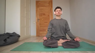 Kulaklıklı genç adam evde meditasyon yapıyor. Odaklanmak için sesli meditasyon. Erkek, sakin müzik dinliyor. Podcast yayını yapıyor, yoga yapıyor. Huzur içinde uyuyor.