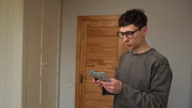 Genç bir adam, mali sorumluluk, bütçe ve refah yönetimini temsil eden yüz dolarlık banknotları dikkatle sayıyor.