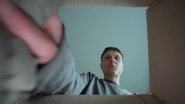 Evde yaşayan ve kıyafetlerini karton kutuya koyan genç bir adam. Yeni bir eve taşınıyorum. Bağış veya geri dönüşüm kavramı