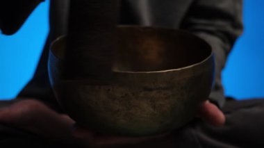 Tibet şarkı kasesini çalan ellerin yakın çekimi loş ışıklı bir odada değişen renkli ışıklarla, derin meditasyon ve enerji iyileştirme atmosferi yaratır.