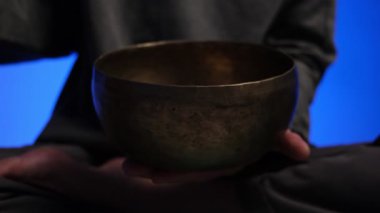 Tibet şarkı kasesini çalan ellerin yakın çekimi loş ışıklı bir odada değişen renkli ışıklarla, derin meditasyon ve enerji iyileştirme atmosferi yaratır.