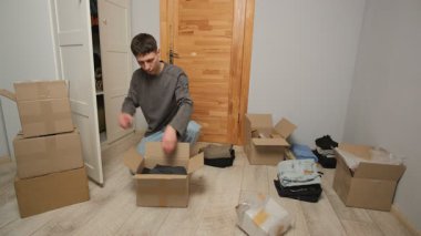 Bir adam büyük bir karton kutuyu açar, dikkatlice giysileri çıkarır ve yeni bir eve taşındıktan sonra düzenler. Çeşitli kutular ve ögeler boşluğu doldurur