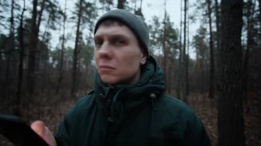 Ormanda kaybolmuş bir adam endişeli görünüyor, çevreyi tarıyor, sonra da navigasyon için telefonunu kontrol ediyor.