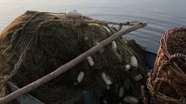 Şamandıralı eski balıkçı ağları ve suya yakın bir teknede ahşap bir kürek, balıkçılık için örülmüş sepetler, geleneksel balıkçılık işçiliği atmosferi yaratıyor.