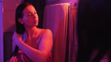 Islak saçlı bir kadın, saçlarını düzeltirken güzelliğine hayran kalıyor. Sıcak, samimi ışıklandırma, dingin ve özgüvenli anı arttırır.