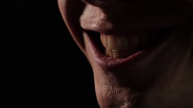 Dramatik düşük aydınlatma, kötü bir gülümseme yakın çekim dudakları ve görünür dişler, karanlık bir ortamda bir gizem, gerilim ve huzursuzluk hissi uyandırır