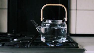 Gaz sobasında ahşap saplı cam bir çaydanlık yavaş çekimde kaynar su. Artan kabarcıklar artan ısıyı gösteriyor. Şeffaf cam kaynama sürecini vurgular.