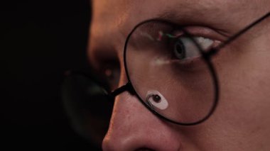 Bir şamdan şemasını yansıtan gözlük takan odaklanmış bir adamın gözleri, karanlık bir oda ortamında kripto para birimini ya da borsa verilerini analiz ederken konsantrasyon. Tüccar dizüstü bilgisayarda çalışıyor.