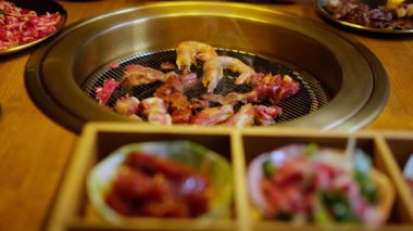 Geleneksel Kore barbekü ızgarasında et. Kore lokantasında ızgara et ve meze. Masa başı ızgarasında et ve karides ızgarası. Masanın etrafında yemek tabakları var..
