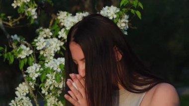 Sezonluk Alerji nedeniyle Hapşıran Genç Kadın. Esmer, Çiçek açan ağacın yanında duruyor ve Burun akıntısından muzdarip. Polene karşı alerjik reaksiyon. Beyaz peçete kullanan hasta beyaz kadın.