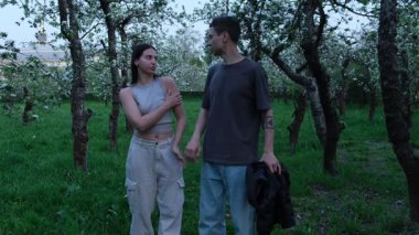 Çiçek açan bahçedeki genç çift. Erkek arkadaşı onu sıcak tutmak için nazikçe kız arkadaşına ceket giydirir. Bahar yürüyüşü sırasında romantik ve şefkatli anlar. Parktaki tarih