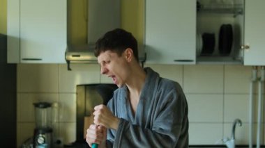 Genç adam mutfak gereçlerini mikrofon olarak kullanıyor ve en sevdiği şarkıyı söylüyor. Mutlu kaygısız adam modern mutfakta yalnız eğleniyor, hafta sonu kahvaltısını hazırlıyor.