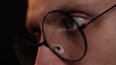 Bir şamdan şemasını yansıtan gözlük takan odaklanmış bir adamın gözleri, karanlık bir oda ortamında kripto para birimini ya da borsa verilerini analiz ederken konsantrasyon. Tüccar dizüstü bilgisayarda çalışıyor.