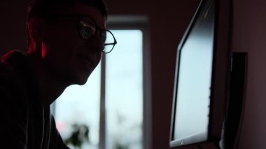 Gözlüklü adam, yatırımlarını, kripto veya borsa çöküşünü, yalnızlığı ve finansal stresi yansıtan loş ışık altında, hayal kırıklığına uğramış bir ifadeyle monitörün önünde oturuyor.