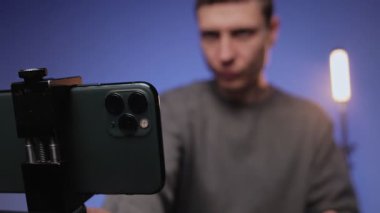 Stüdyoda veya evde video çeken erkek blogcu, çevrimiçi video kaydediyor. Akıllı telefon kullanan bir adam. İçerik yaratıcısı eğlence kanalında canlı yayın yapıyor. Renkli RGB ışıklandırması