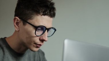 Dizüstü bilgisayarda çalışırken boynu ağrıyan bir adam. Rahatsiz çalisma pozisyonu boyun incinmesine neden oluyor. Gri arka planda siyah gömlekli bir ofis çalışanı.