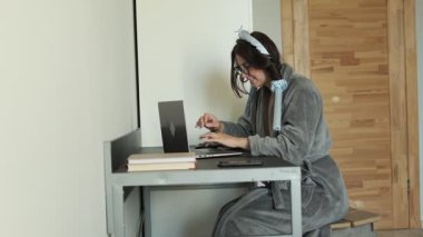 Bornoz ve bigudi giymiş hayal kırıklığına uğramış bir kadın evde dizüstü bilgisayardan temel bilgisayar becerilerini öğrenmeye çalışıyor.