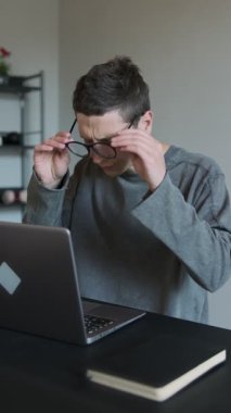 Evdeki yorgun adamın bilgisayarın başında otururken gözlük çıkarması, dijital göz yorgunluğu ya da uzun ekran zamanının yorgunluğunu göstermesi. Ofis sendromu konsepti. Dikey video