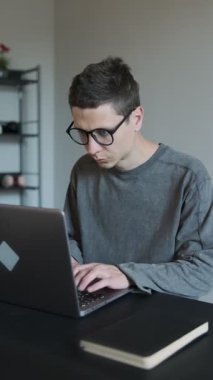 Dizüstü bilgisayarla çalıştıktan sonra masadan kalkarken sırtı ağrıyan gözlüklü genç adam.