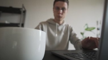 İçişleri Bakanlığı 'ndaki bir bardaktan kahvesini yudumlayan adam bilgisayarlı bir masanın arkasında. Freelancer rutini. Gün ışığı, ev içi..