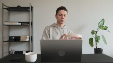 Ev ofis masasında kitaplık ve bitkiyle bilgisayarla çalışırken kulaklık takan odaklı bir adam. Freelancer üretken çalışma için müzik açıyor