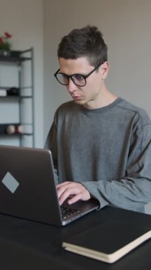 Dizüstü bilgisayarda çalışırken boynu ağrıyan bir adam. Rahatsiz çalisma pozisyonu boyun incinmesine neden oluyor. Gri arka planda siyah gömlekli bir ofis çalışanı.