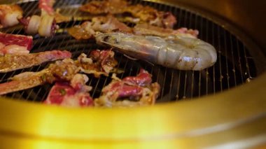 Çeşit çeşit çiğ et ve altın kenarlı geleneksel barbekü ızgarasında büyük bir karides pişirme.