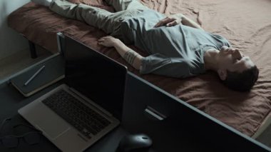 Yorgun ve serbest çalışan biri yatağa uzanır ve çalışmaya devam edemez. Dizüstü bilgisayar ve gözlük masada dinleniyor. Ev ofis ortamında serbest çalışmanın, iş hayatında dengesizliğin ve duygusal yorgunluğun gerçekçi bir tasviri..